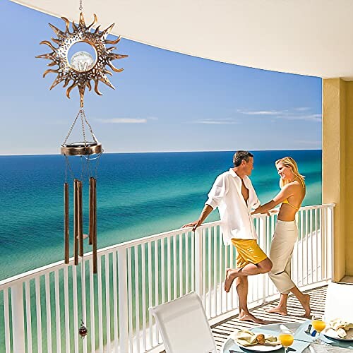 Couple enjoying ocean view on balcony with sun-themed wind chime.