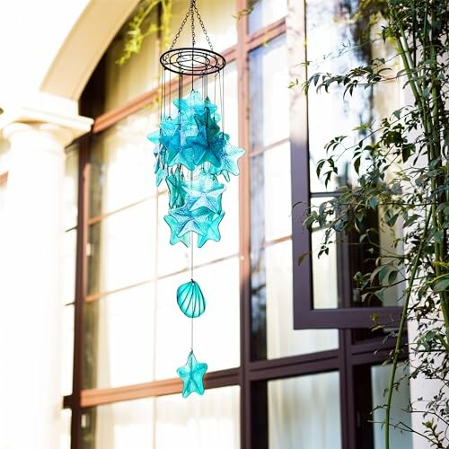 Blue star-shaped wind chime hanging outdoors near a window.