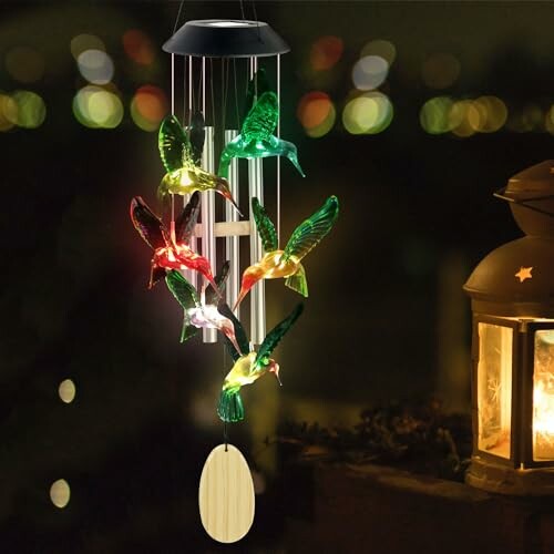 Colorful hummingbird wind chime with glowing lights at night.