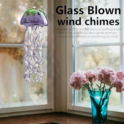 Glass blown wind chimes near a window with flowers in a vase.