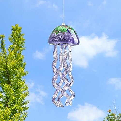 Glass jellyfish wind chime hanging outdoors against a blue sky.