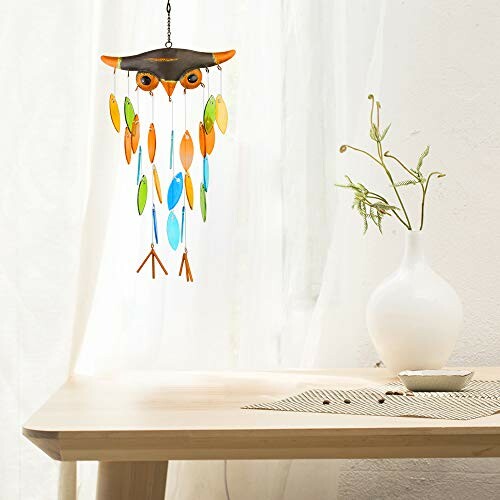 Owl wind chime hanging above a wooden table with a white vase.