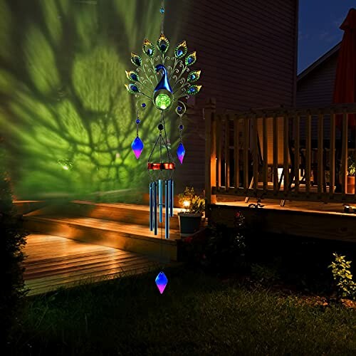 Peacock wind chime with colorful lights on a deck at night.