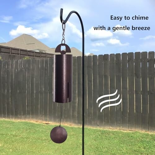 Wind chime hanging in a garden with a fence and blue sky background.