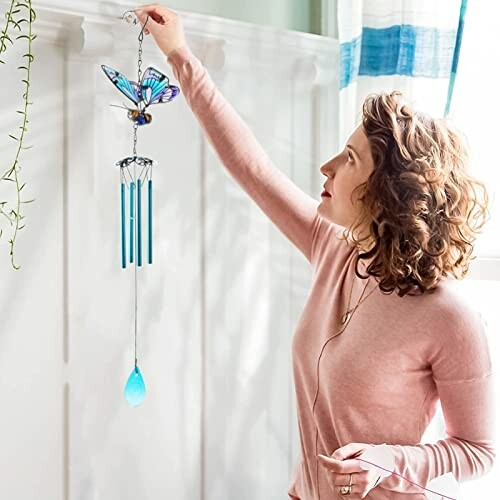 Woman hanging a butterfly wind chime indoors.